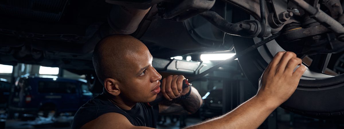 Ilustrační stock: technik při prohlídce osobního automobilu v autoservisu, vozidlo na zvedáku, kontrola podvozku, civilně, bez loga STK