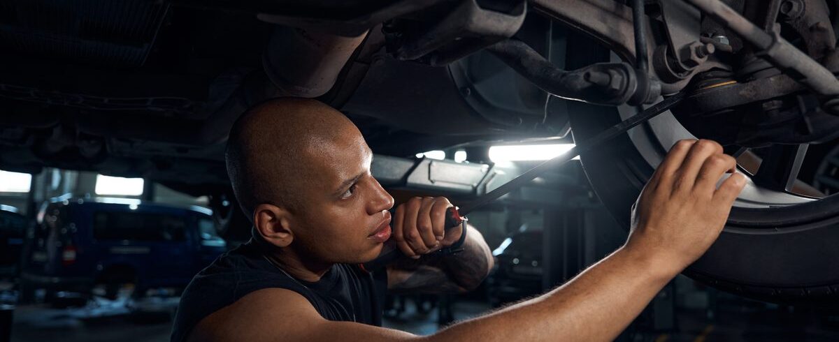 Ilustrační stock: technik při prohlídce osobního automobilu v autoservisu, vozidlo na zvedáku, kontrola podvozku, civilně, bez loga STK