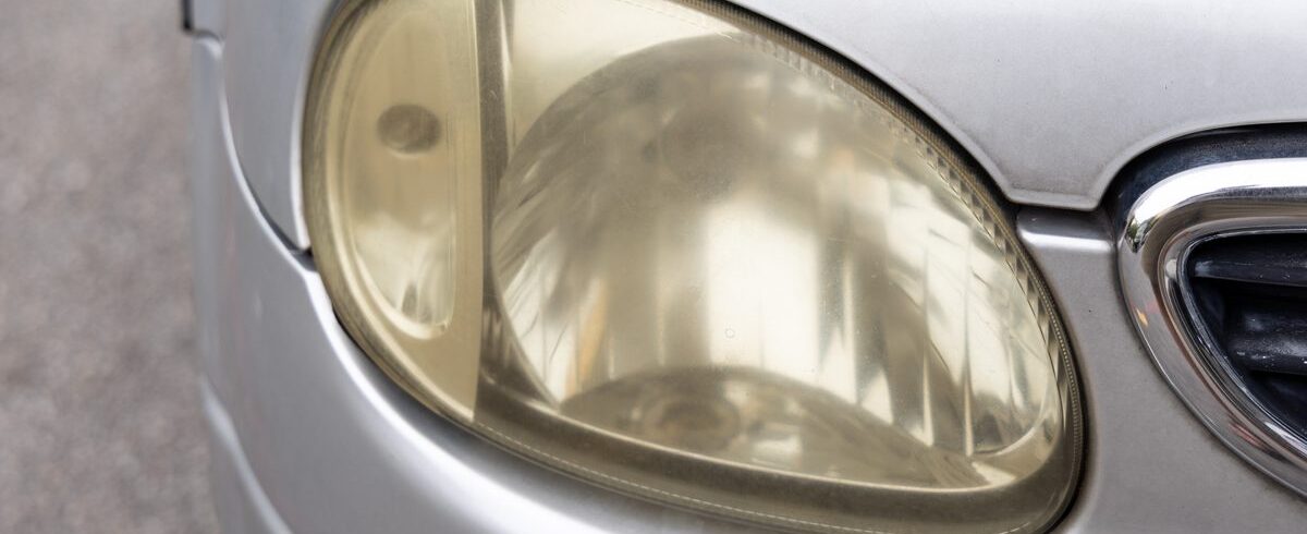 Ilustrační stock: zakalený světlomet osobního automobilu s matným polykarbonátovým krytem, detail předního reflektoru s viditelným zežloutlým povrchem bez loga výrobce